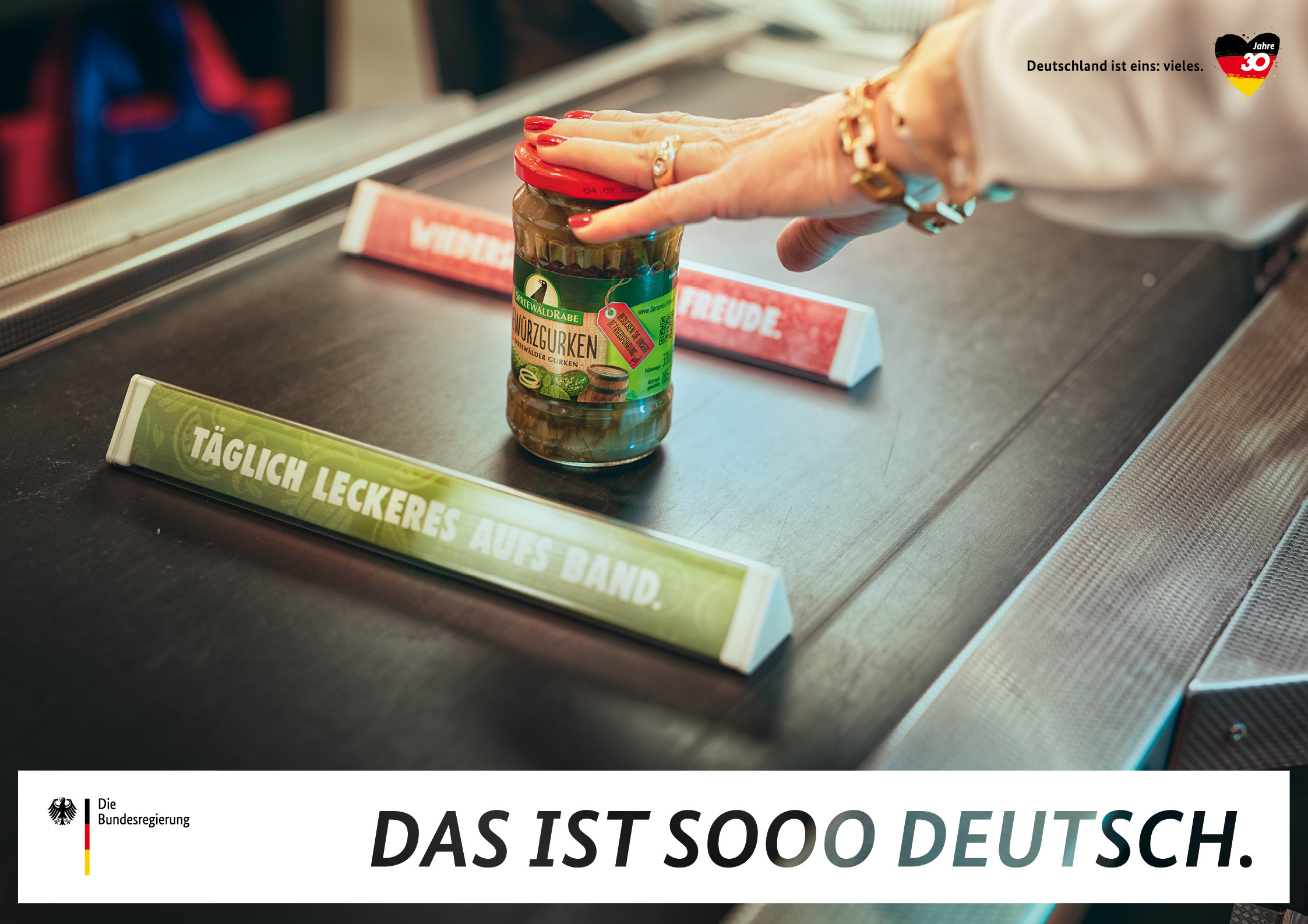 Ein Kassenband mit Warentrennern und Gurkenglas auf einem Plakat der Kampagne "Deutschland ist eins: vieles".