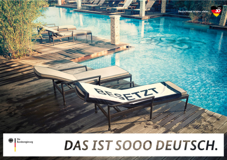 Liegestühle am Pool, von einem Handtuch besetzt, auf einem Plakat der Kampagne "Deutschland ist eins: vieles".