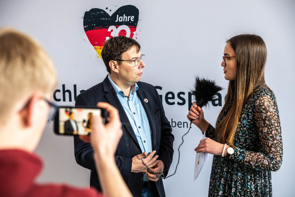 Eine Schülerreporterin interviewt vor dem Logo von 